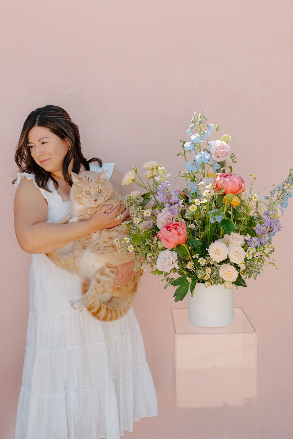 Pastel flower arrangement with peonies and roses next to Redlands florist, Stephanie Centeno, and a cat.